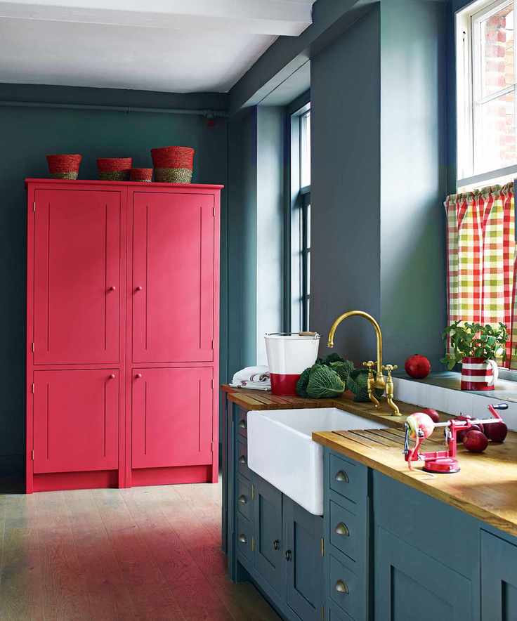 A blue grey kitchen with bright red painted freestanding cabinet and colorful gingham blinds.