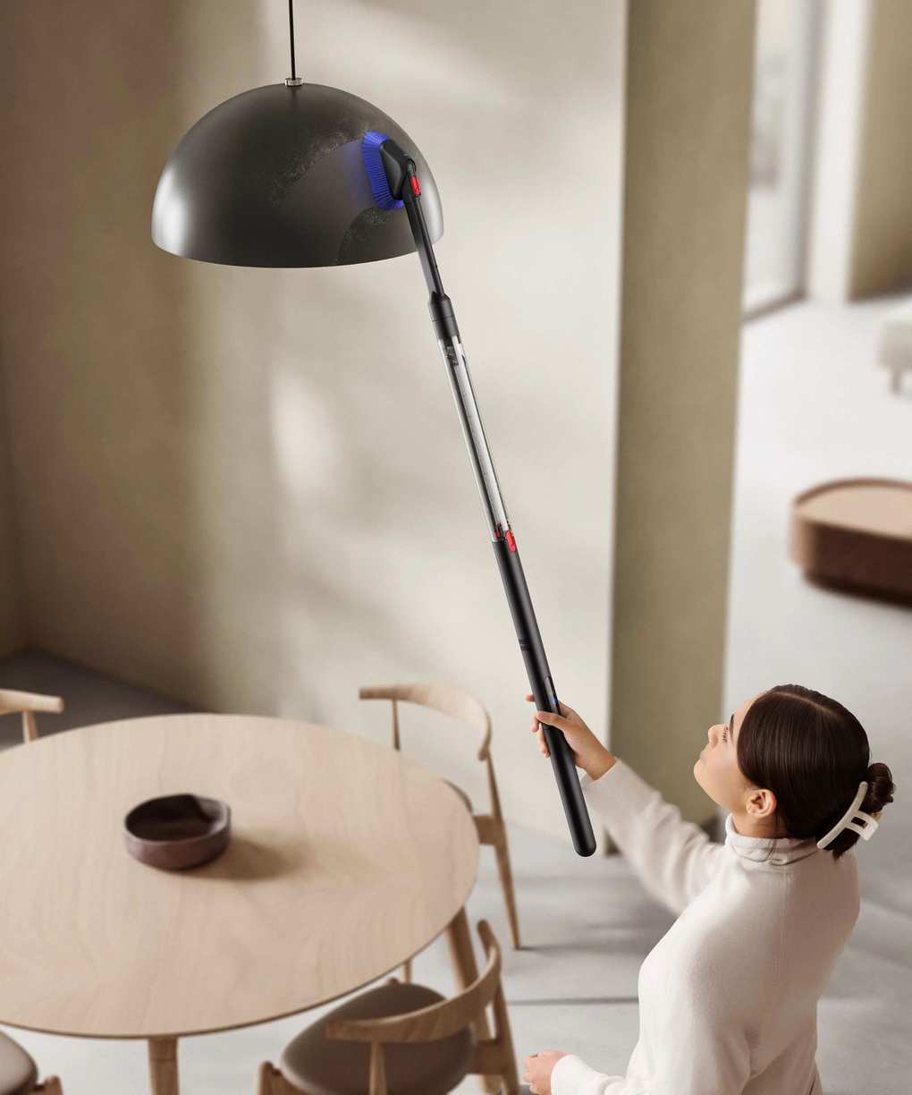 Dyson PencilVac cleaning a hanging light with dusting brush attachment, held above head