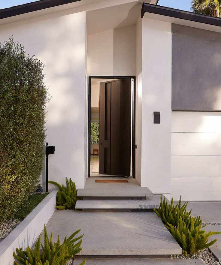 A modern, white home with sleek steps leading to an open, black front door