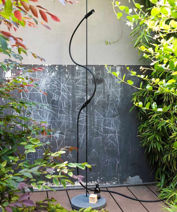 A simple black freestanding outdoor shower surrounded by trees and bushes for privacy