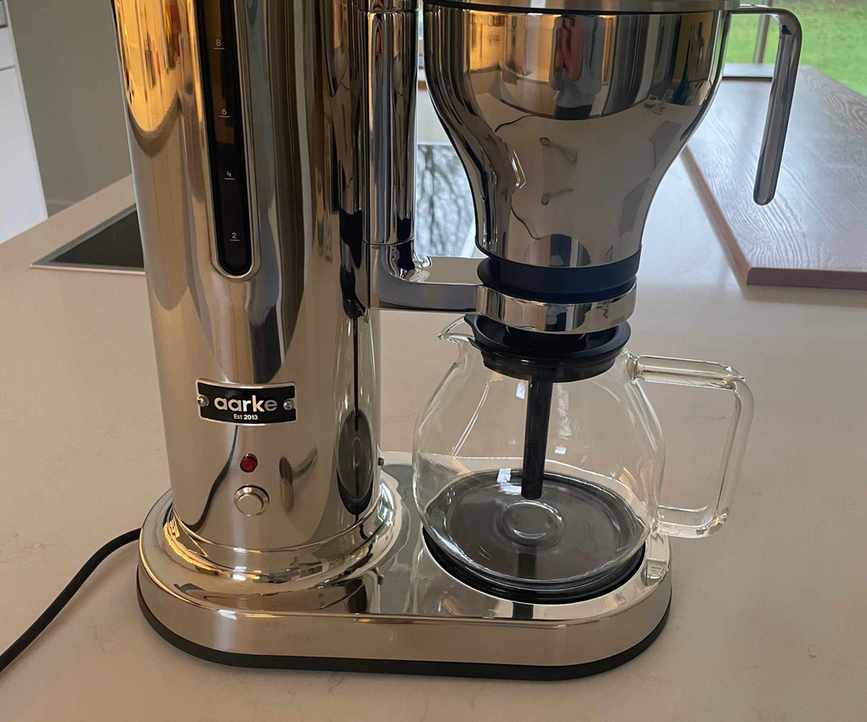 A stainless steel drip coffee maker on a white counter top.