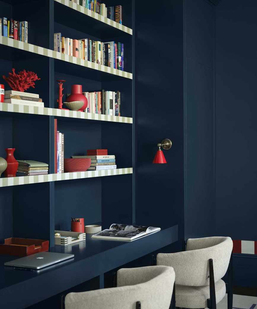 home office with dark blue color-drenched walls, shelving with books and decor, and desk space