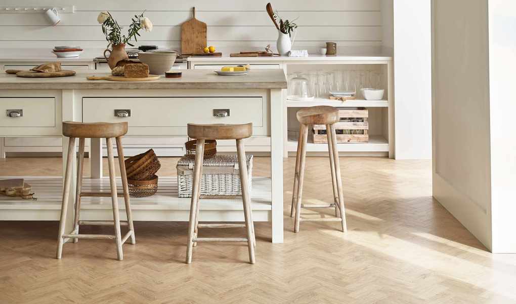 Light wood-look vinyl flooring in a stylish white kitchen with wooden stools.