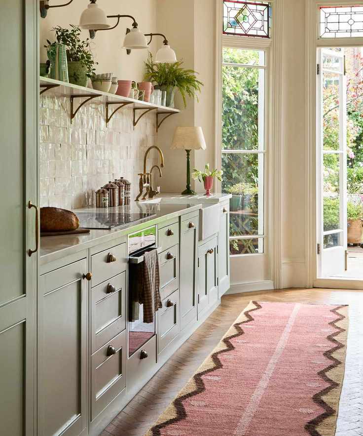 Kitchen featuring sage green cabinets, cream backsplash, and pink rug