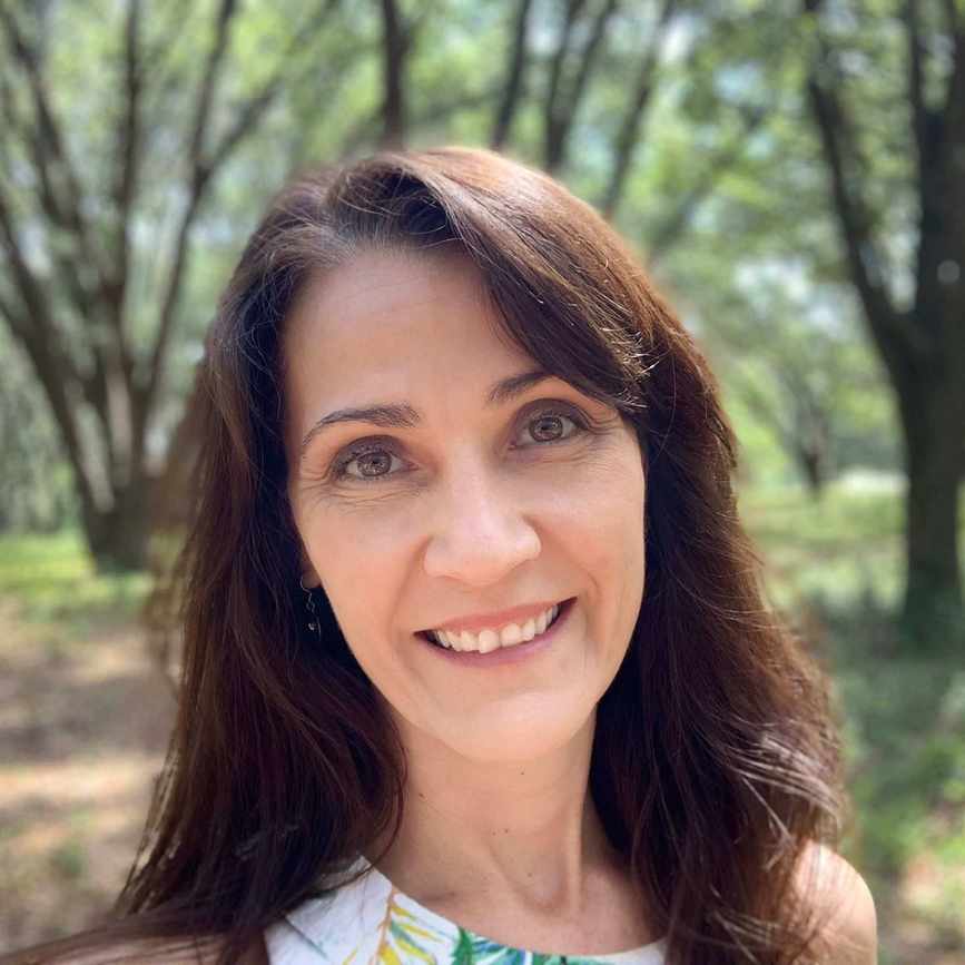 A headshot of Jennifer Pressimone with a blurred forest landscape behind.
