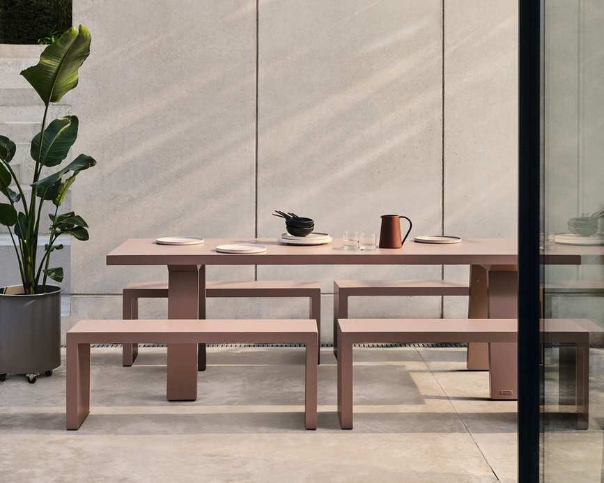A pale pink outdoor dining table and bench seats on a contemporary paved terrace
