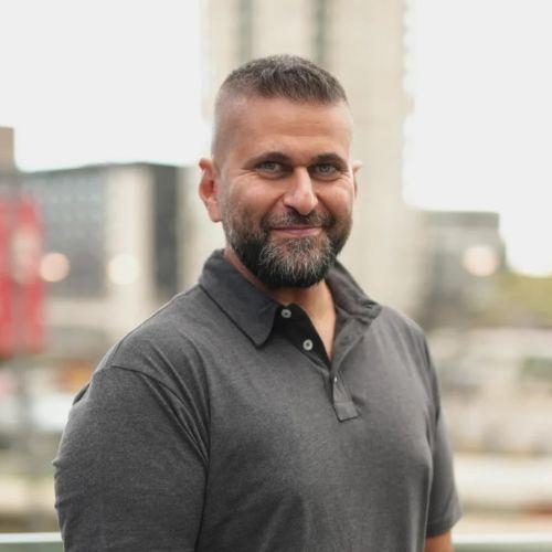 Headshot of Michael Zohouri in a gray polo, standing in front of a blurred city backdrop.