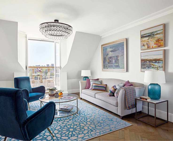 Small living room lighting ideas in a white loft living room with blue armchairs, neutral sofas and rooftop views.