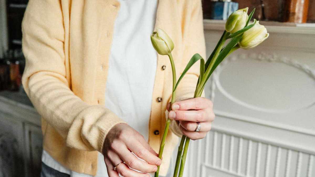 Woman in yellow cardigan holding three pale green tulips