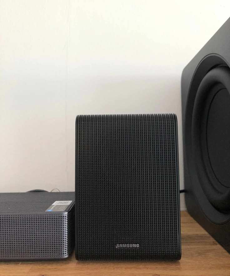 Closeup of surround speaker of Samsung HW-QS750F soundbar on wooden shelf in Dan Fauzi's home.