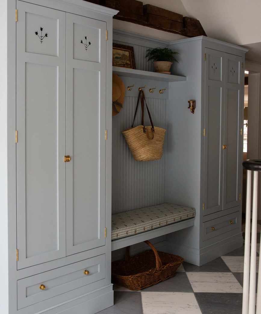 Pale cornflower blue mud room cabinet storage in an open entryway with checked floors and brass fixtures