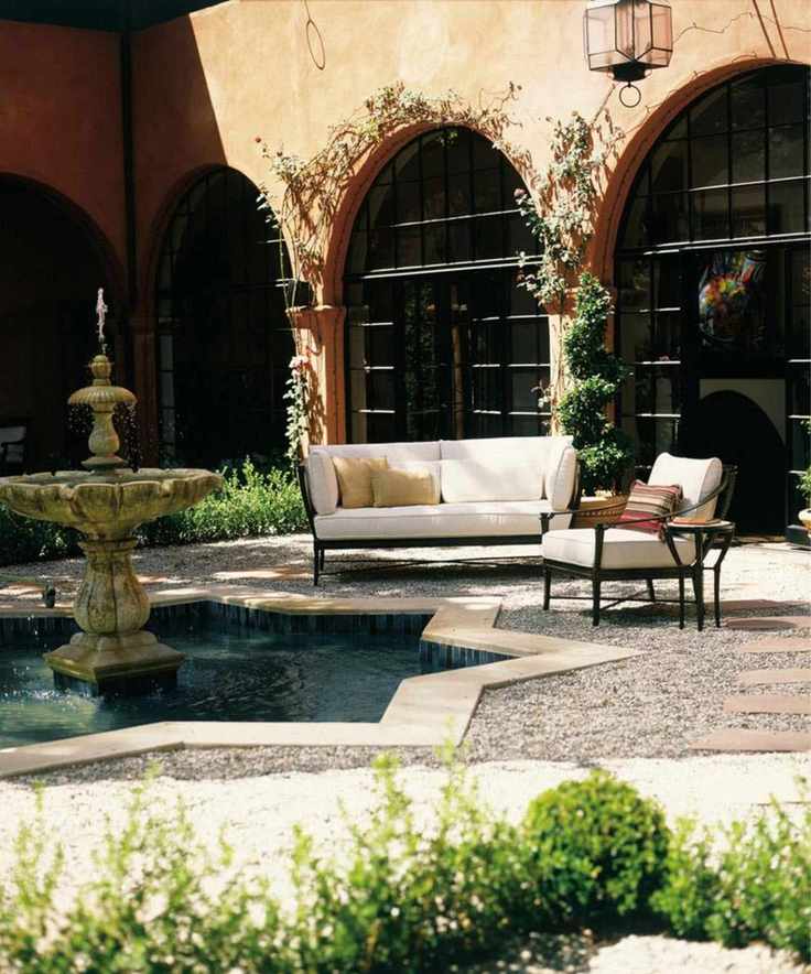 european inspired outdoor space with terracotta arched walls and wrought iron furniture sat by a large outdoor fountain