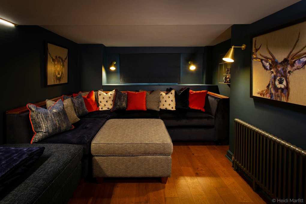 movie room with navy sectionals, gray patterned footstool, hardwood floor, wall lights, blind, decorative cushions