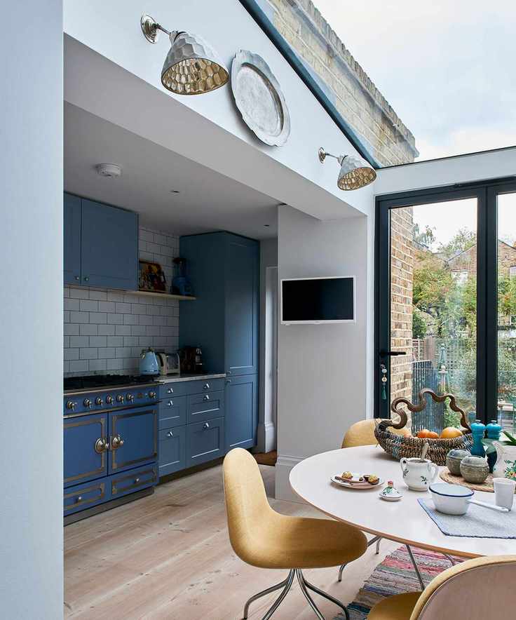 Kitchen wall lighting ideas with industrial lamps, blue cabinetry and a round table with yellow chairs.