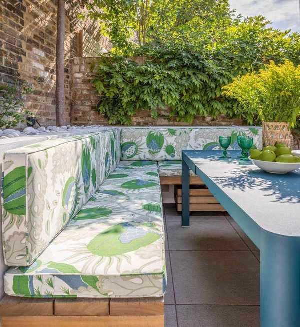 a walled garden with a wooden banquette seat and floral upholstered bench cushions iwth blue dining table