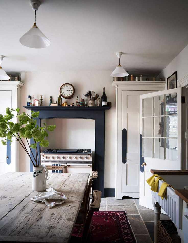 Cream kitchen with a classic cream stove, navy blue painted fireplace and rustic wooden dining table.