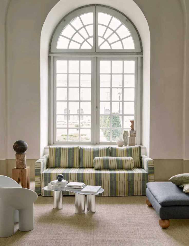 Modern living room design in traditional interior, sofa with striped upholstered covers, armchairs and lounge chairs working with sofa to create a sociable seat space, large arch window