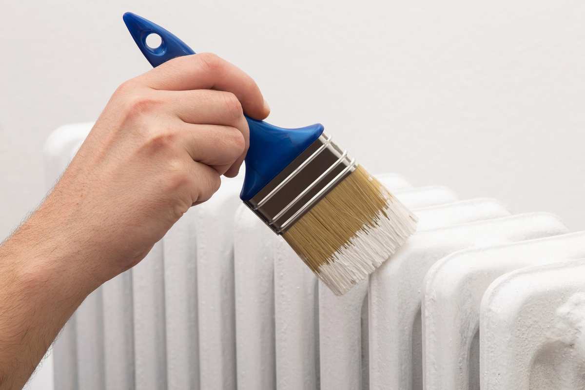 Someone using a brush to paint a radiator white