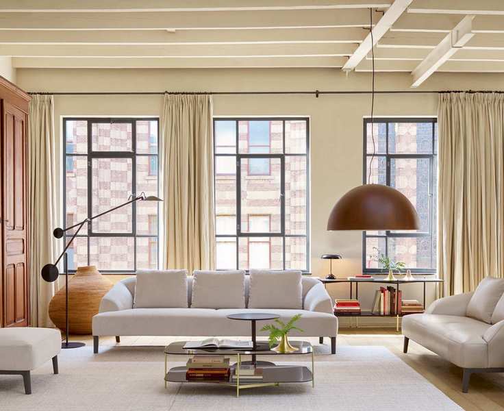 An example of how to plan living room lighting, with white sofas, black floor lamps and a large pendant light in front of three large windows.