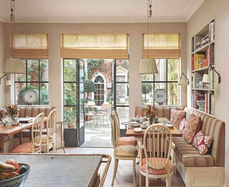 A bright breakfast nook with built-in banquette seating, decorative pillows, and expansive glass doors that lead to a flourishing garden courtyard