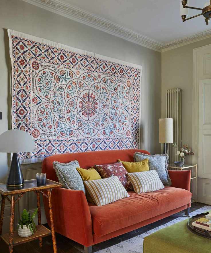 A soft blue painted living room with a velvet orange couch and a large wall hanging suzani.