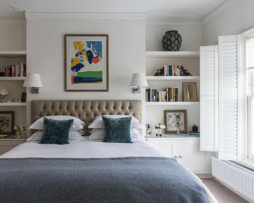 Master bedroom with a double bed and padded headboard. Fitted shelves and window with shutters.