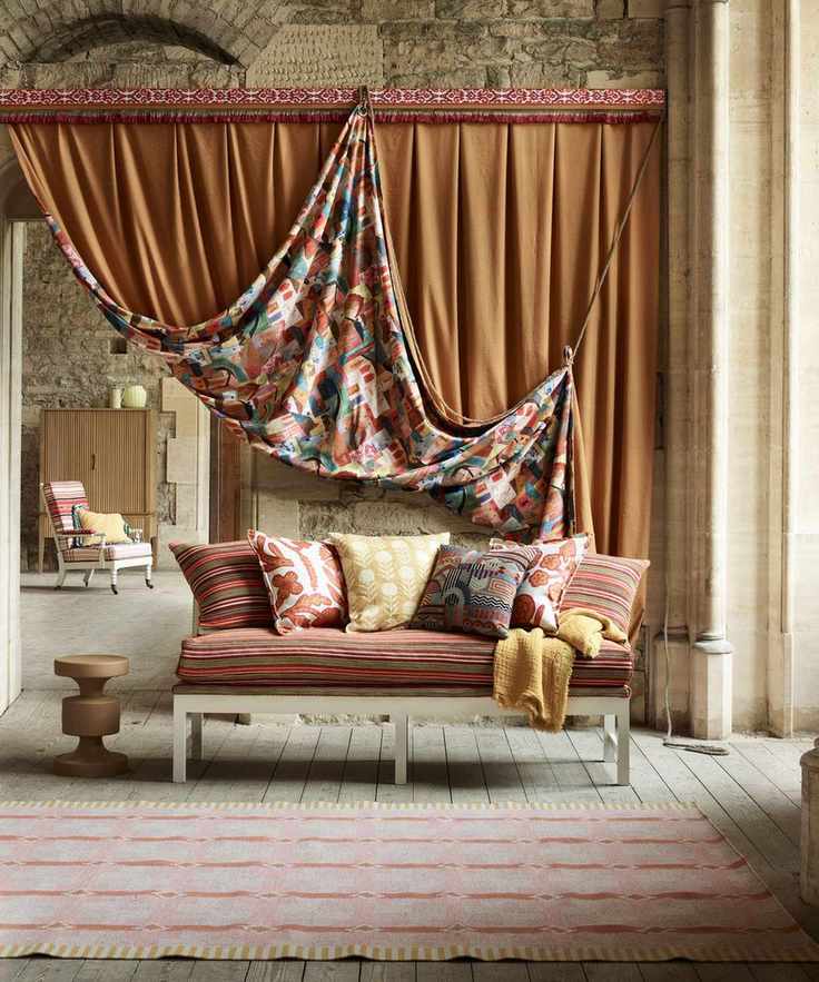An example of broken plan living room ideas showing a sofa with cushions in warm tones in front of a large textile drape used to separate two areas
