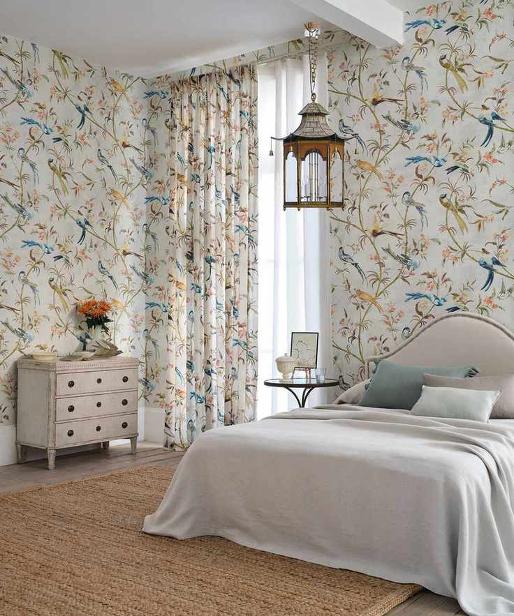 Large bedroom with matching floral patterned curtains and wallpaper, bed with upholstered headboard, hanging lantern light, natural textured rug