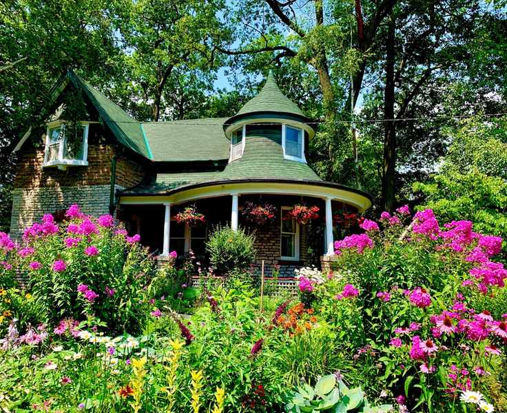 An example of south facing garden ideas showing a period house behind a large flower bed full of pink and yellow plants