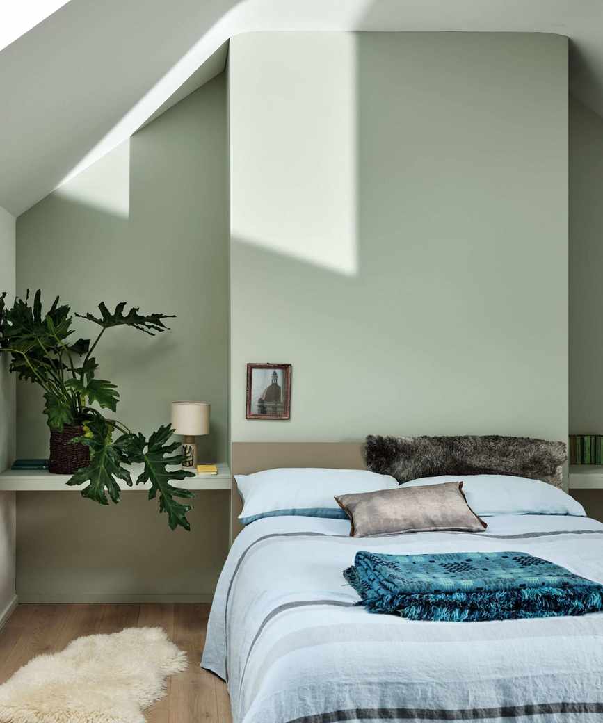 A peaceful green bedroom with blue bedding is mostly in shade, but the top left shows streaks of bright sunshine