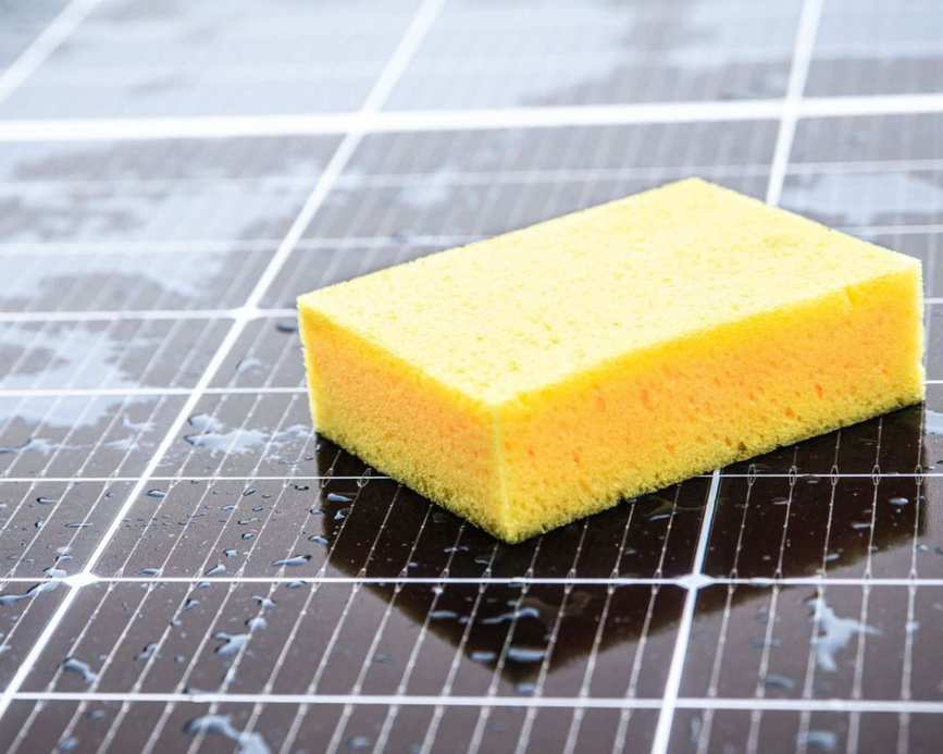 A person cleaning a solar panel with a yellow sponge.
