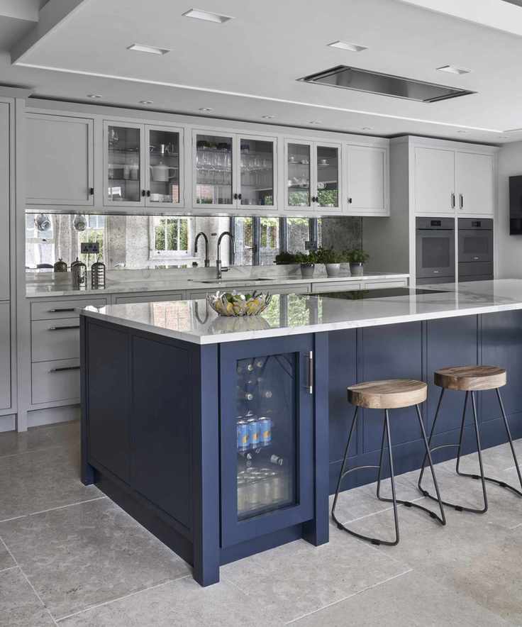 A kitchen with a large blue island, featuring a drinks fridge and brown leather bar stools.