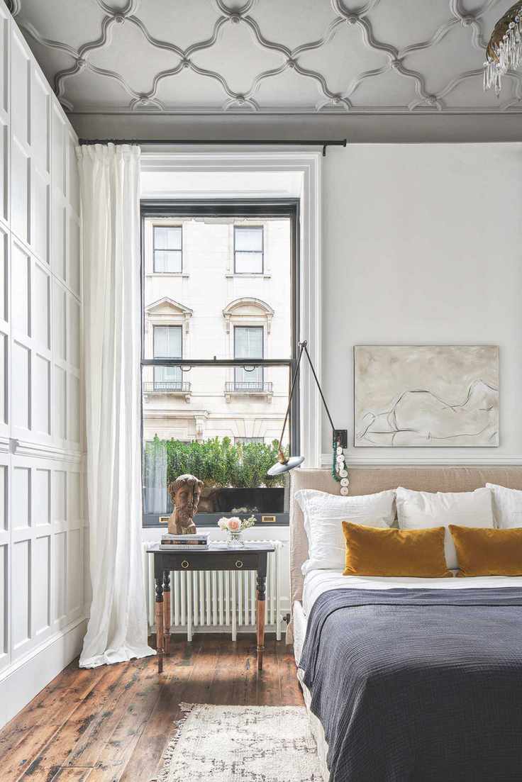 white bedroom with black accents, wooden floor, black throw, mustard cushions, wall light, artwork, decorative ceiling, panelled walls, desk