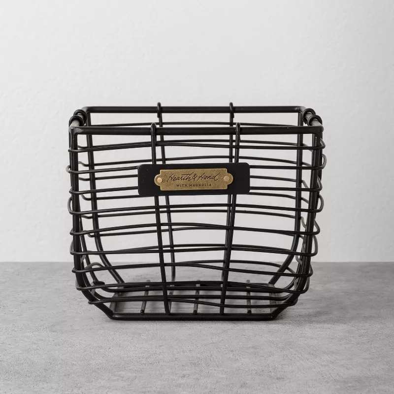 A black wire storage basket with a brass label tag on the front.