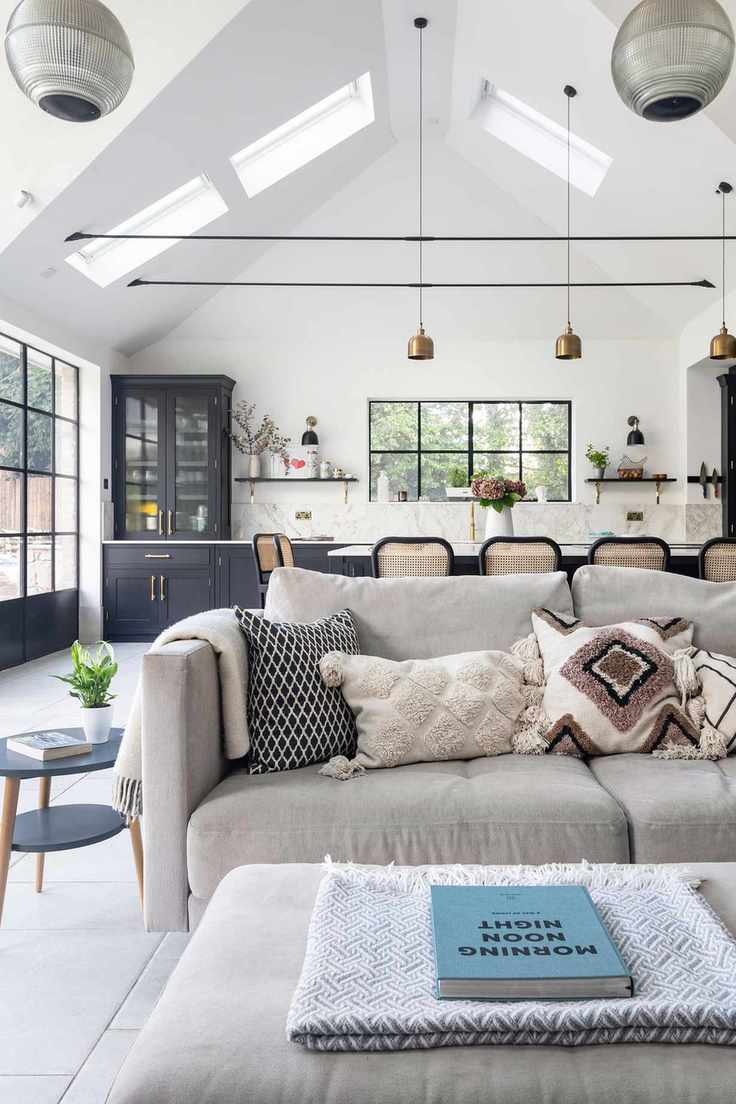 white sofa in open plan kitchen with steel framed windows and vaulted ceiling and gray kitchen cabinets behind