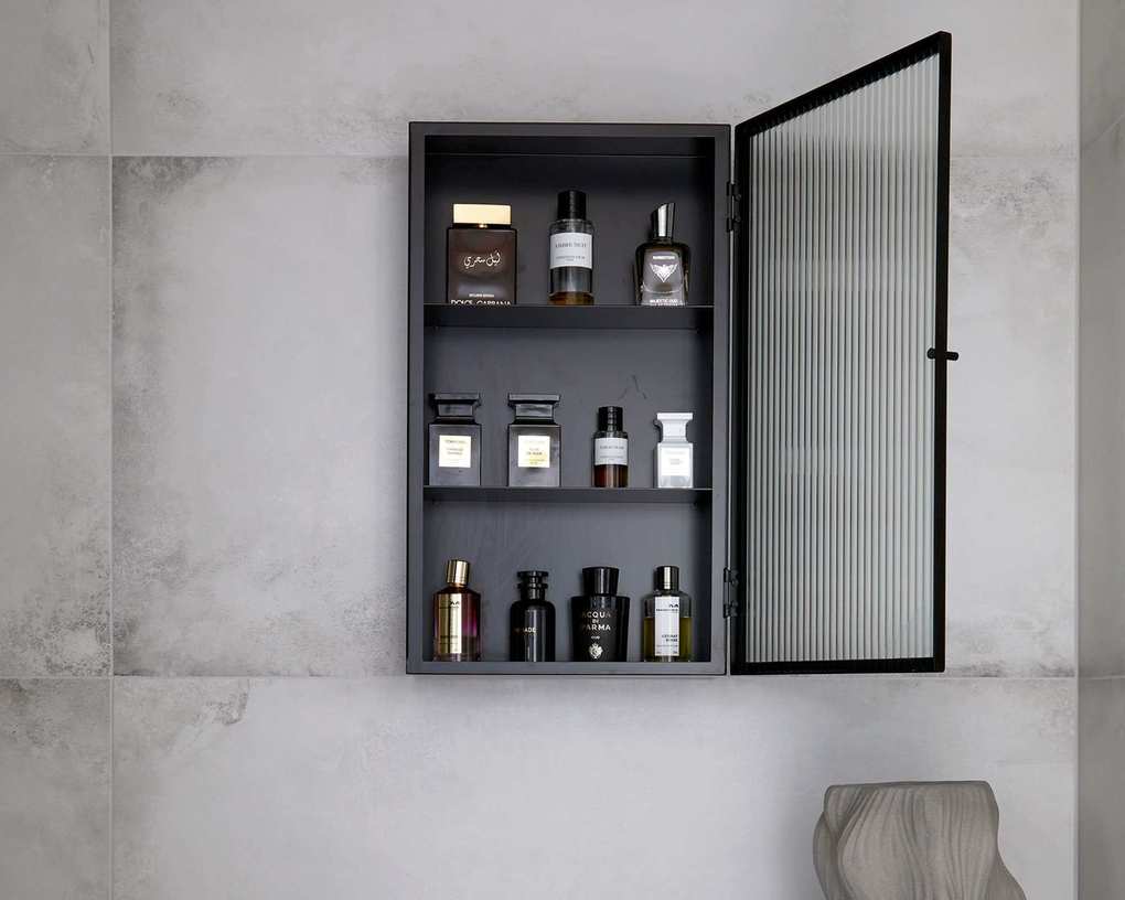 A black wall mounted wall cabinet with glass perfume bottles inside, an open fluted glass door