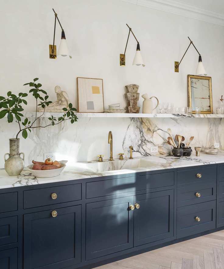 Gold wall lights over a blue kitchen unit with marble countertops.