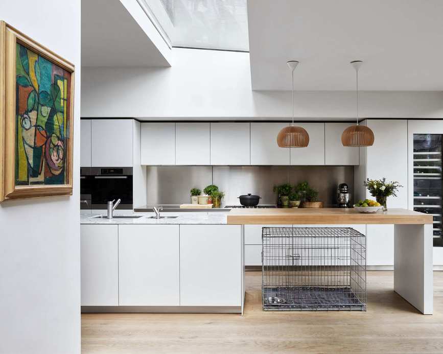 Airy and angular kitchen with kitchen island in white on wood flooring looking out on garden with French doors and painting on wall