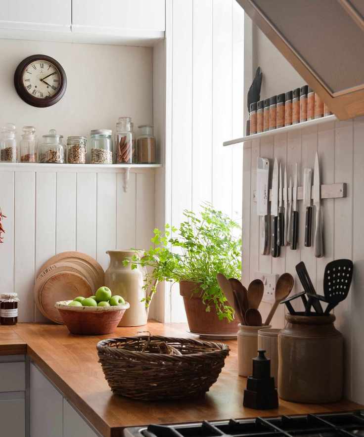 A rustic style kitchen, with plants on the window sill, knives hanging on the wall, and a woven basket on the counter