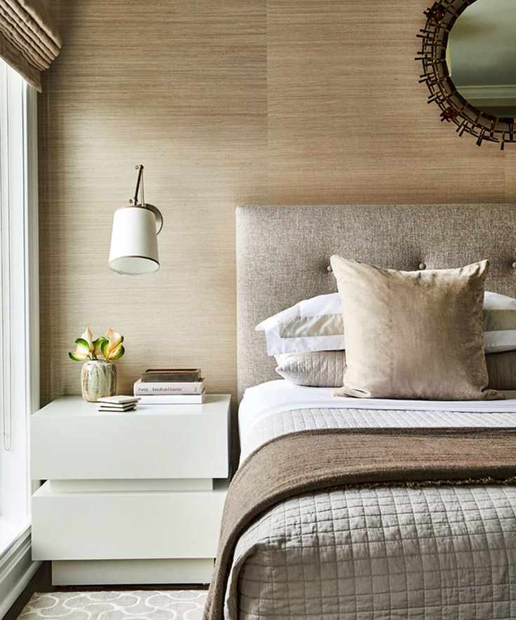 Modern bedroom with neutral brown and beige color scheme. Layered bedding, wall lamp above beside table.