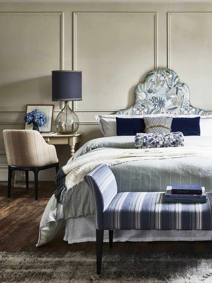blue and white bedroom with taupe walls, blue and white bedding, footstool, wooden floors, blue lamp, armchair, side table
