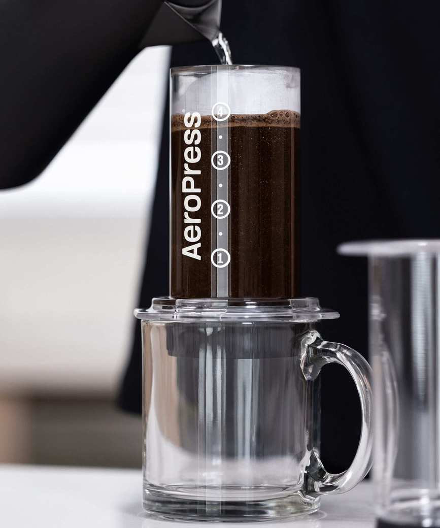 A clear AeroPress brewing coffee over a clear cup