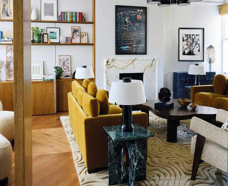 a modern white living room with toffee colored velvet sofas, textured rug, marble tables and a wooden bookcase to the right