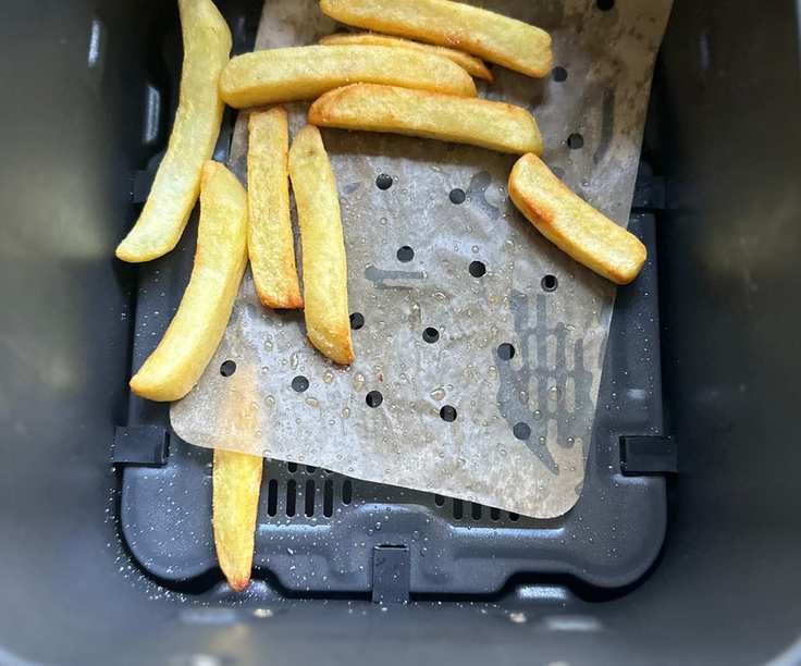 A handful of thick fries on top of a perforated paper air fryer liner inside a black air fryer basket.