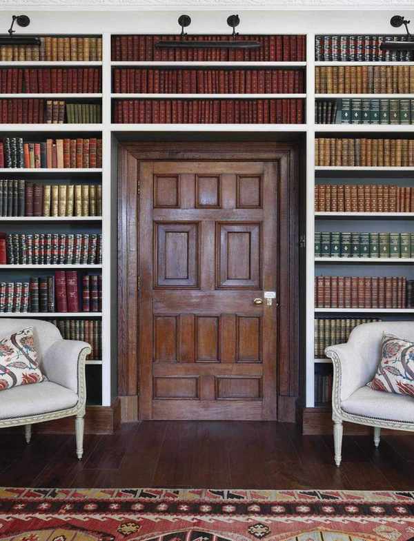 Wooden door with book shelving at either side and above and two armchairs with wood floor and rug