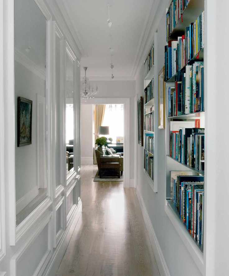 White hallway with built in shelving books mirrored panels suspended spot lighting wooden flooring leading to living room