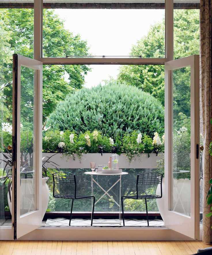 An example of south facing garden ideas showing a balcony with a bistro table and chairs set and and large, round bush in front