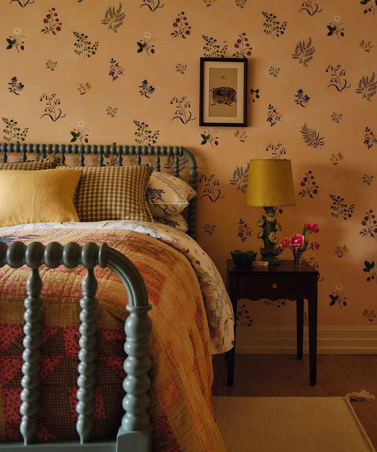 a floral wallpapered bedroom with a green bobbin bedframe and layered plaid bed linens