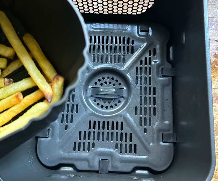 A clean, empty air fryer basket with a silicone air fryer basket liner filled with fries visible to the side.