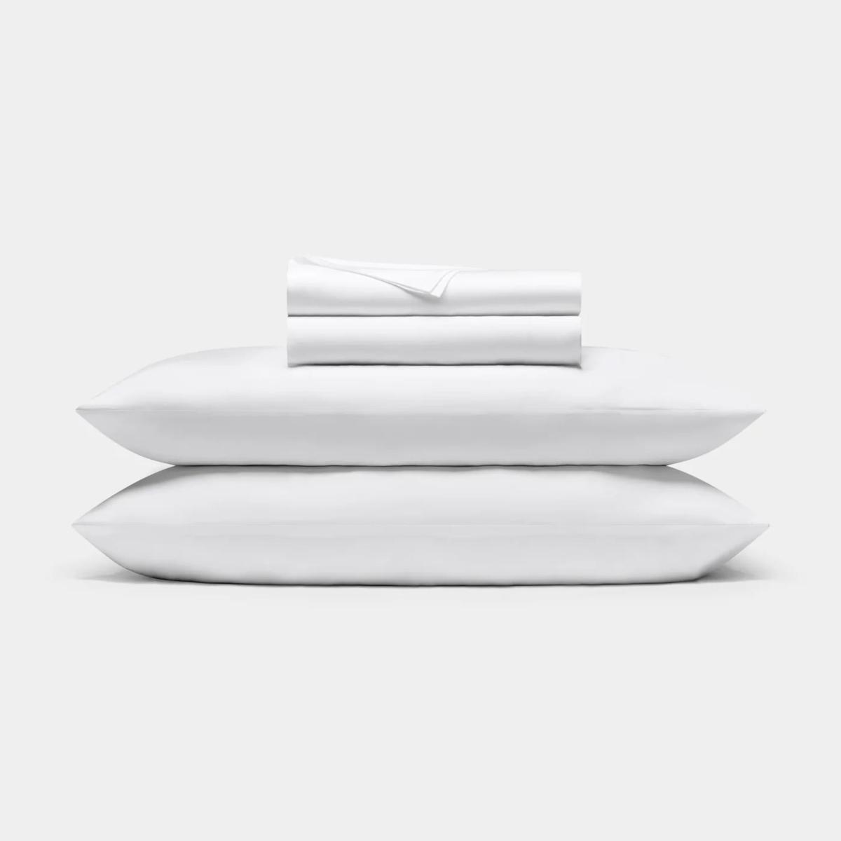 A white pillowcases shown on two piled pillows with folded sheets on top.